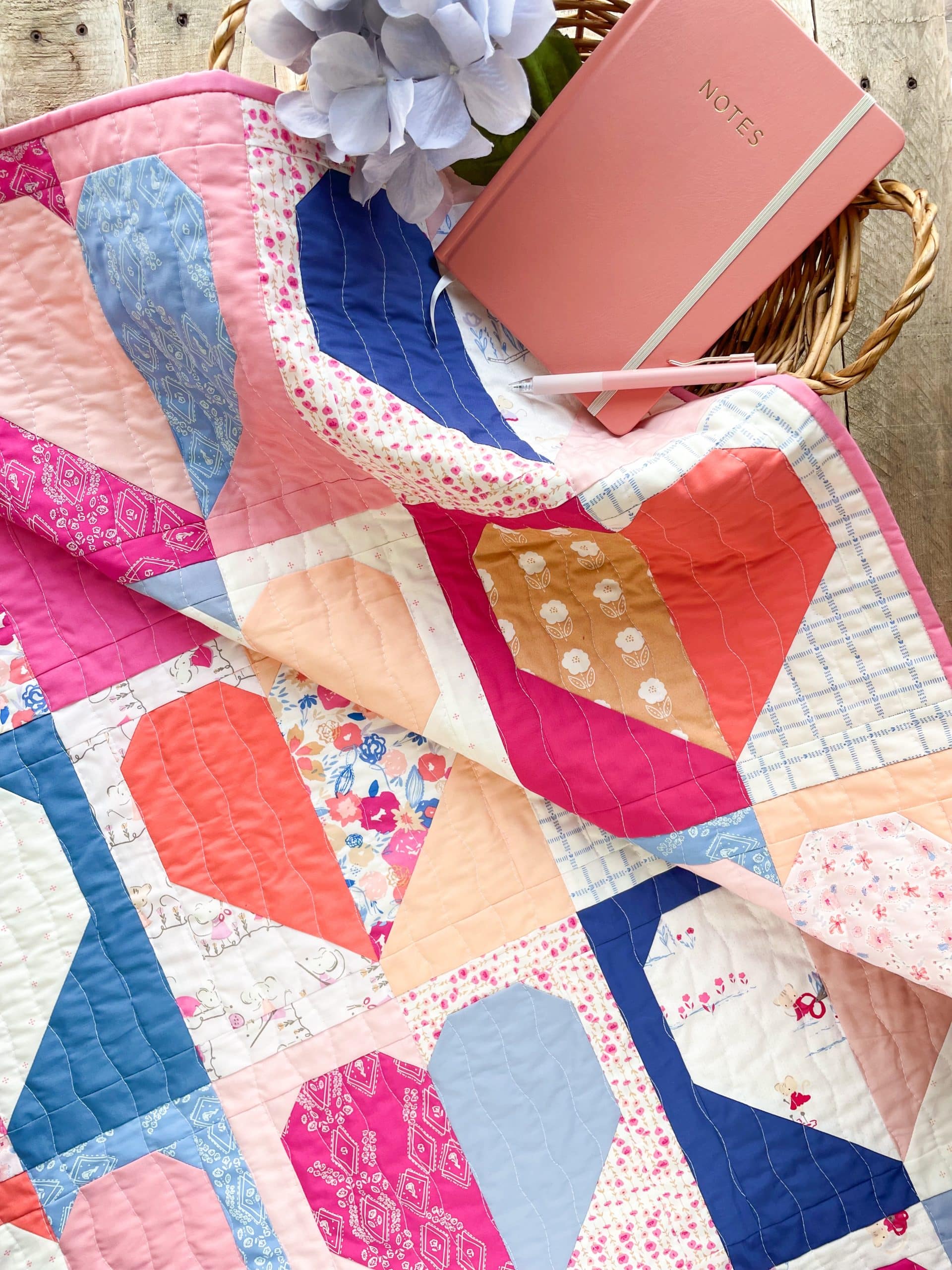 Colorful quilt with pink notebook and pen.