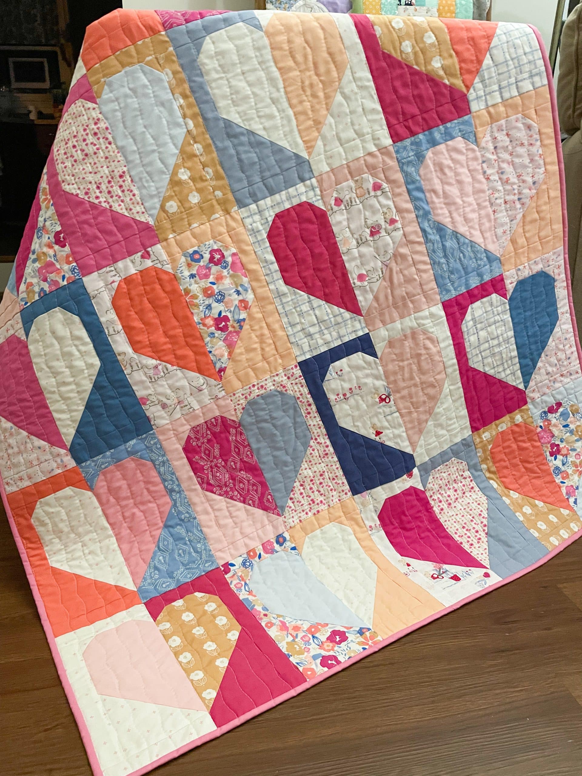 Colorful handmade heart quilt on a wooden floor.