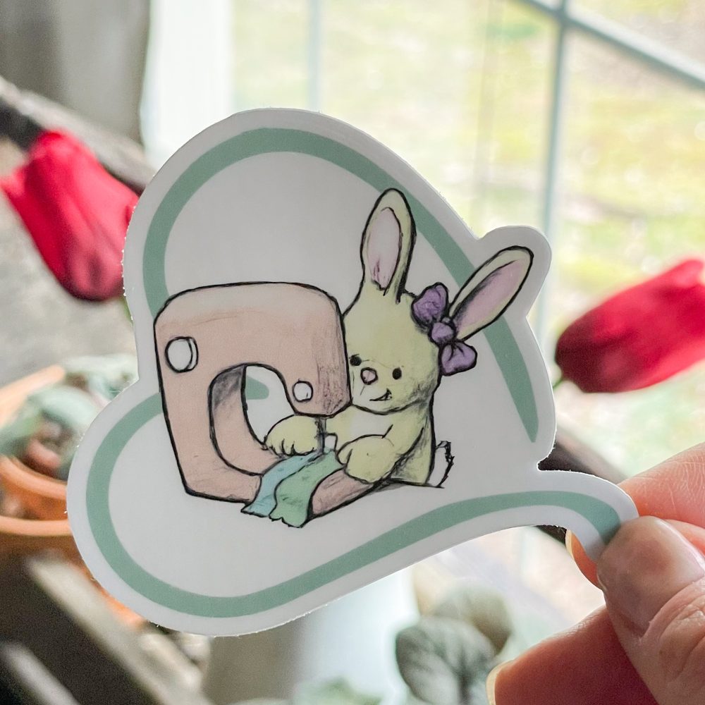 Sticker of bunny sewing with a machine.