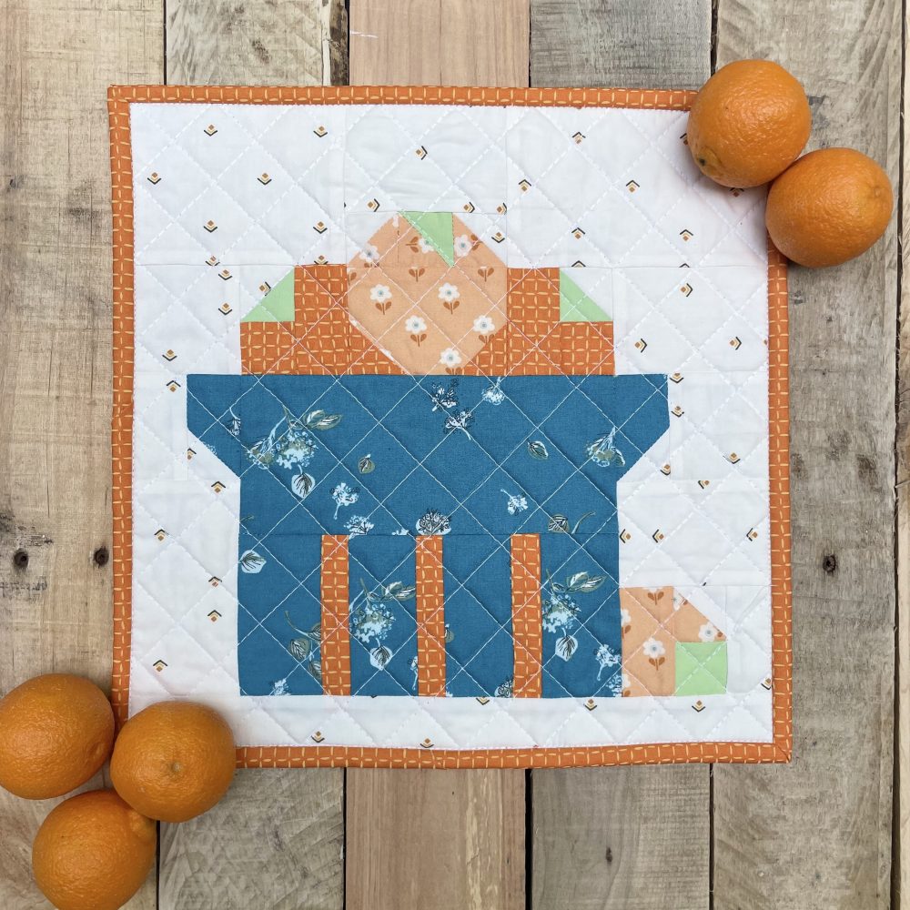 Colorful quilt square with oranges on wooden background.