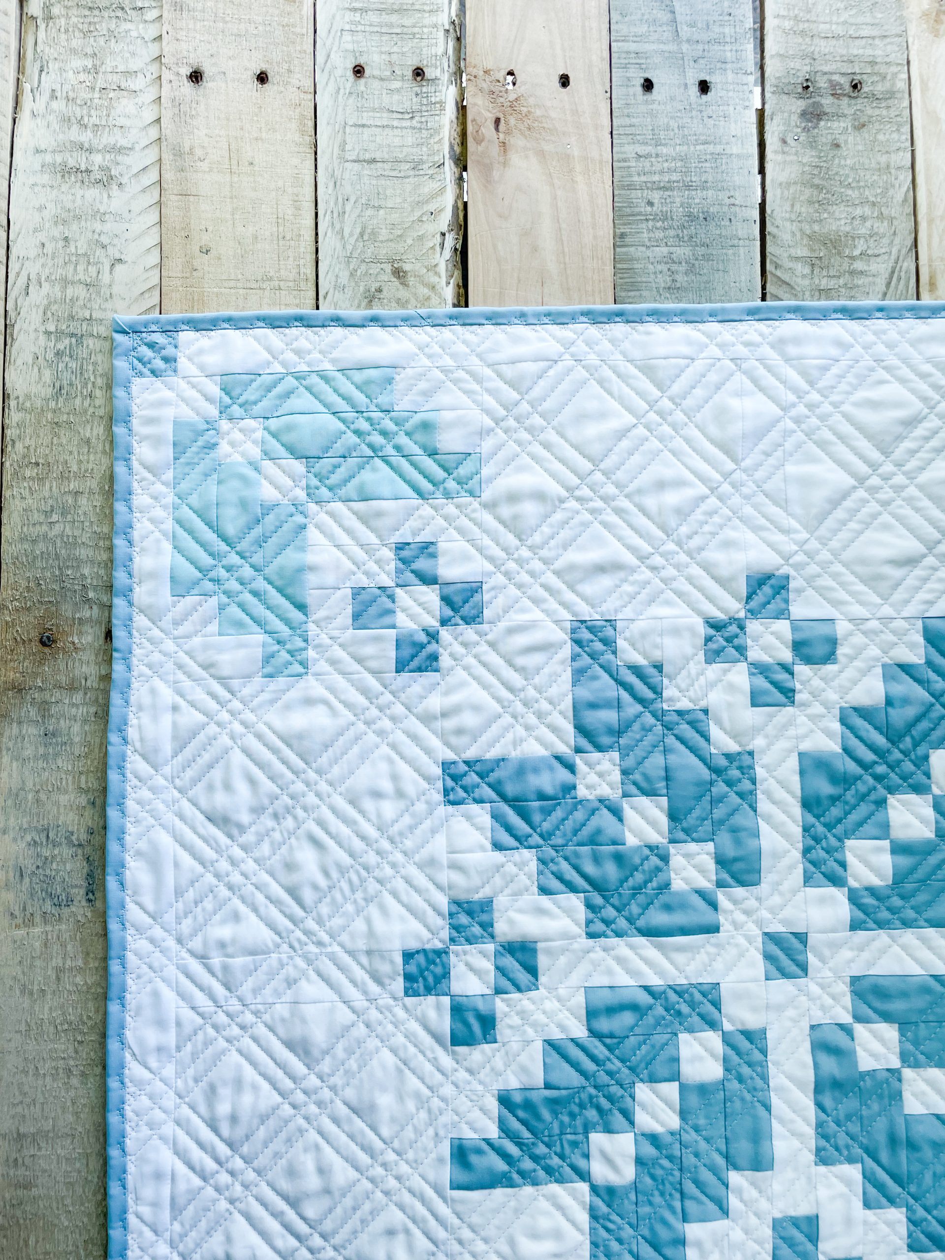 Blue and white quilt against wooden fence